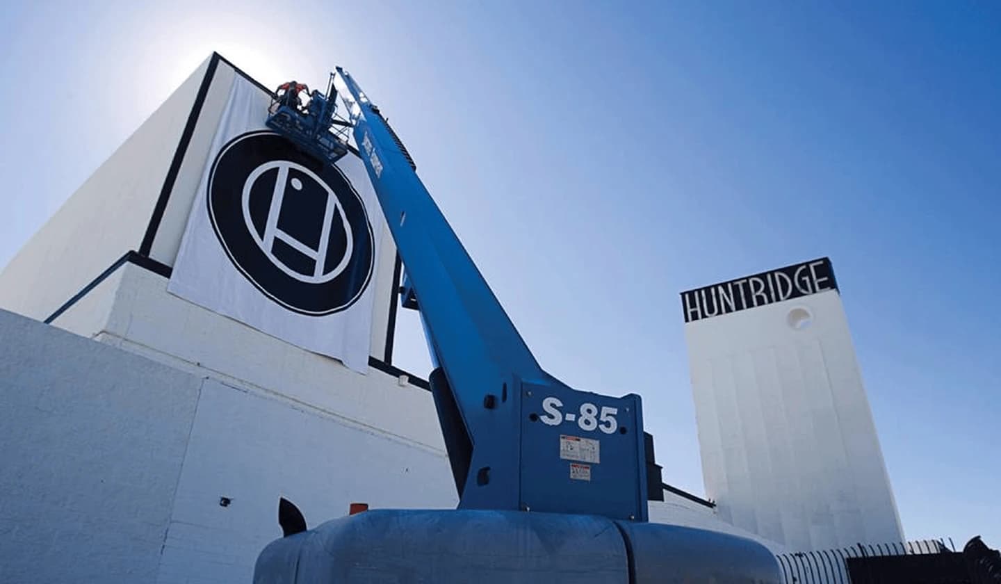 Huntridge brand banner being installed by a crane against a clear blue sky.