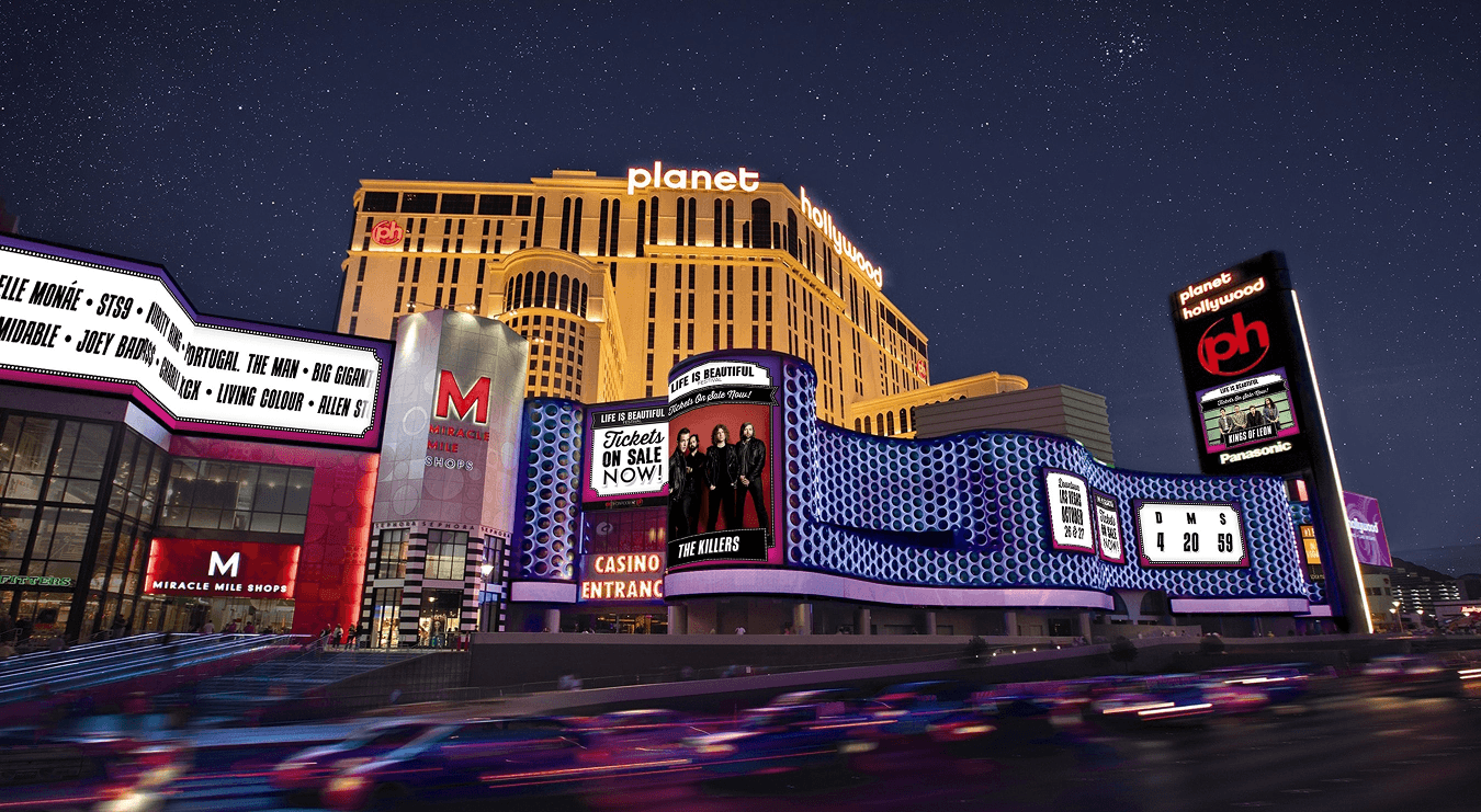 The Las Vegas Strip at night with the Planet Hollywood marquee carrying a giant Life is Beautiful and Killers ticket banner across the building, neighboring casinos lit behind it.