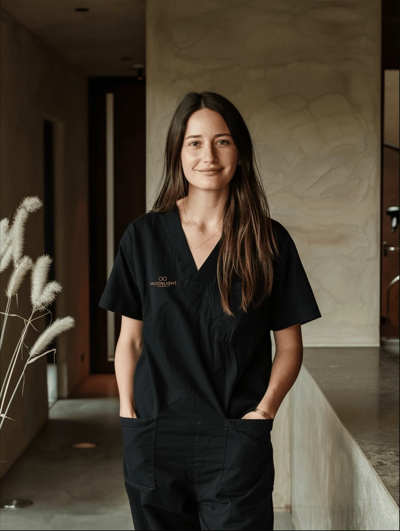 A practitioner in branded Moonlight Longevity scrubs, photographed in the practice's plaster-walled interior.